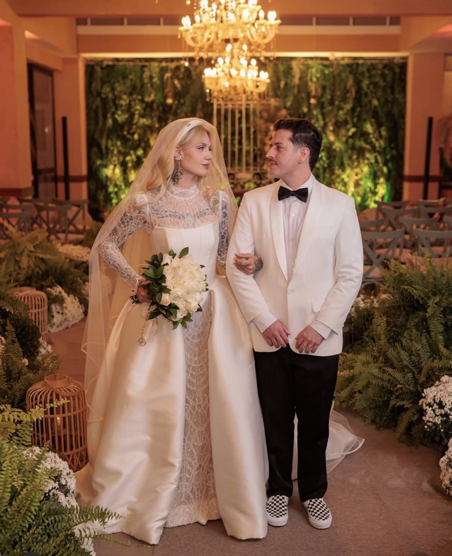 Casal de noivos na capela, diante da parede verde e dos lustres