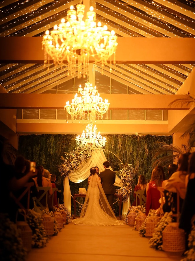 Cerimônia à noite sob os lustres, com o casal no altar e os convidados