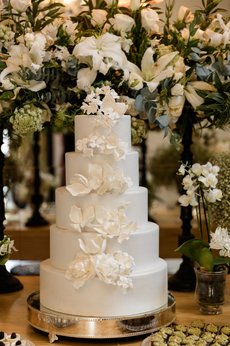 Bolo de casamento de cinco andares com flores de açúcar, sob arranjos brancos